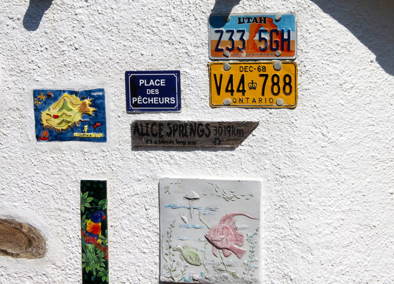 A textured white wall featuring license plates, artistic tiles, and directional sign.